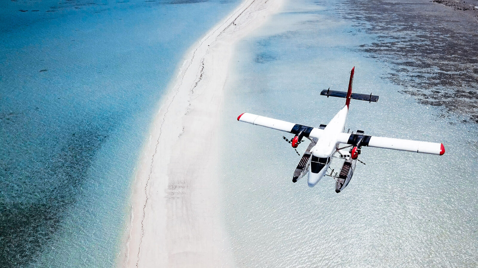 A seaplane flying low over a sandbank and shallow reef